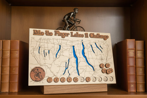 Wooden map of the Bike the Finger Lakes Challenge with engraved lakes and wooden tokens on a bookshelf