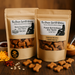 Two packages of handmade organic dog treats from 'The Chosen Spot K9 Kitchen - Bacon Cheddar Biscuits With Duvall Farms Bacon and Peanut Butter Bones in kraft bags with piles of treats in front on a nuetral brown background.