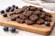 Beef + Blueberry Bites, handmade organic dog treat on a light wooden cutting board, blueberries and chia seeds nearby on a neutral background.