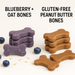 A stack of Gluten-Free Peanut Butter Bones and a stack of Blueberry + Oat Bones. Handmade organic dog treats from 'The Chosen Spot K9 Kitchen' with treats displayed in front along with blueberries and whole grain oats.