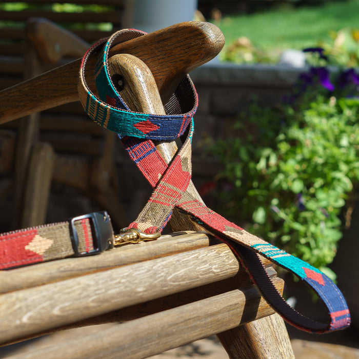 A hand-woven cotton collar and leash set in National Parks Sequoia patterns from a tail we could wag brand sitting in the sun on a wooden outdoor rocking chair.
