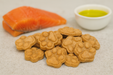 Salmon Paws. Handmade organic dog treats from The Chosen Spot K9 Kitchen on a light background with a slice of salmon and a dish of olive oil.