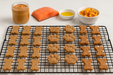  Peanut Butter Bones, Salmon Paws and Bacon Cheddar Biscuits with Duvall Farms Bacon Handmade organic dog treats from The Chosen Spot K9 Kitchen on a cooling rack with a white background.