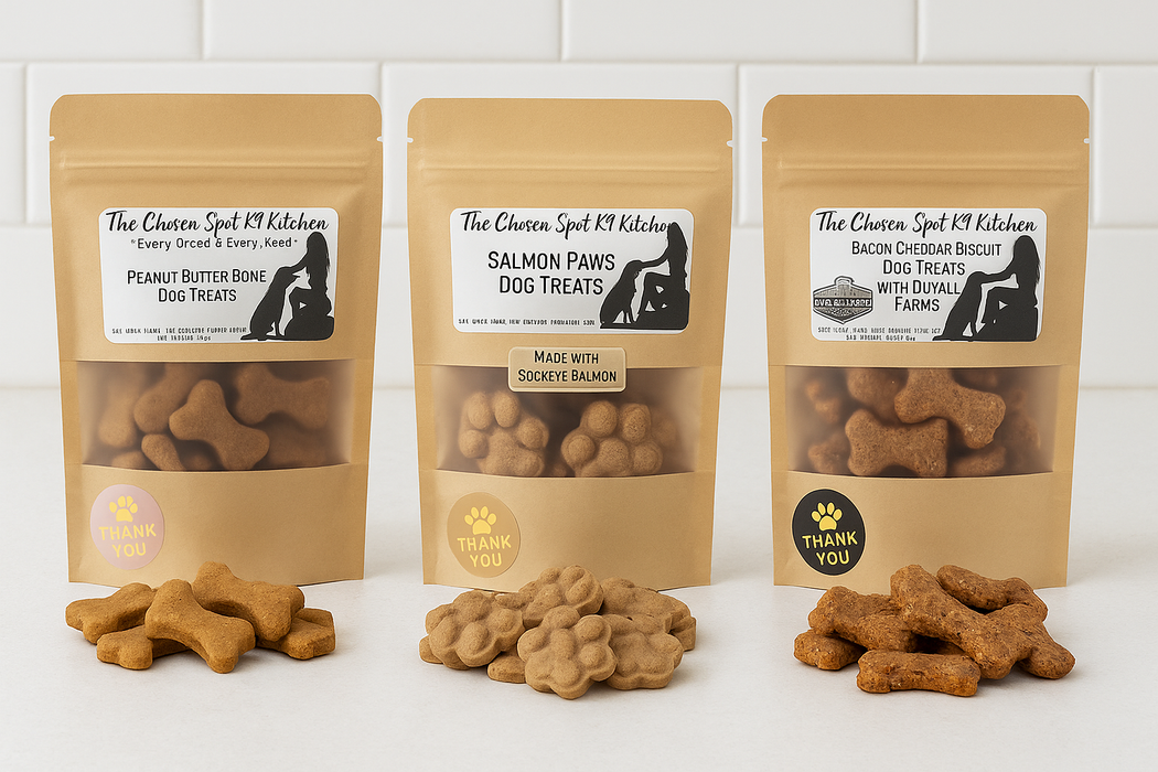 Three packages of 'The Chosen Spot K9 Kitchen' dog treats, Peanut Butter Bones, Salmon Paws and Bacon Cheddar Biscuits with Duvall Farms Bacon on a beige background. Handmade organic dog treats.