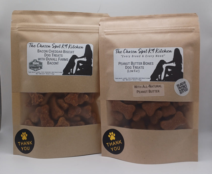 Two packages of handmade organic dog treats, one labeled 'Bacon Cheddar Biscuits' and the other 'Peanut Butter Bones', from The Chosen Spot K9 Kitchen.