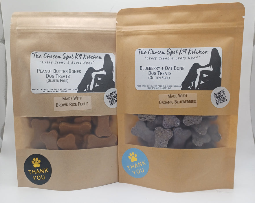 Two packages of handmade organic dog treats, one labeled 'Peanut Butter Bone' and the other 'Blueberry Oat Bone', from The Chosen Spot K9 Kitchen.