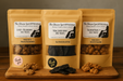 Packages of Salmon Paws, Veal Liver Jerky and Liver + Blueberry Paws handmade organic dog treats from The Chosen Spot K9 Kitchen on a wooden board with a dark background.