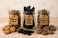 Three mason jars filled with Salmon Paws, Veal Liver Jerky, and Liver + Blueberry Paws from The Chosen Spot K9 Kitchen with piles of corresponding treats on a wooden surface.