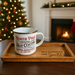 Mug with 'North Pole Original Hot Cocoa' text on a wooden tray in front of a Christmas tree and fireplace.