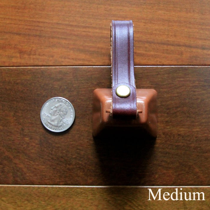 cowbell with antique brass finish and burgundy bridle leather strap shown next to a quarter