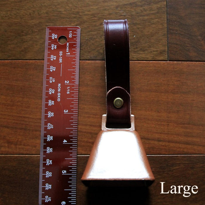 cowbell with antique brass finish and burgundy bridle leather strap shown next to a quarter and a ruler