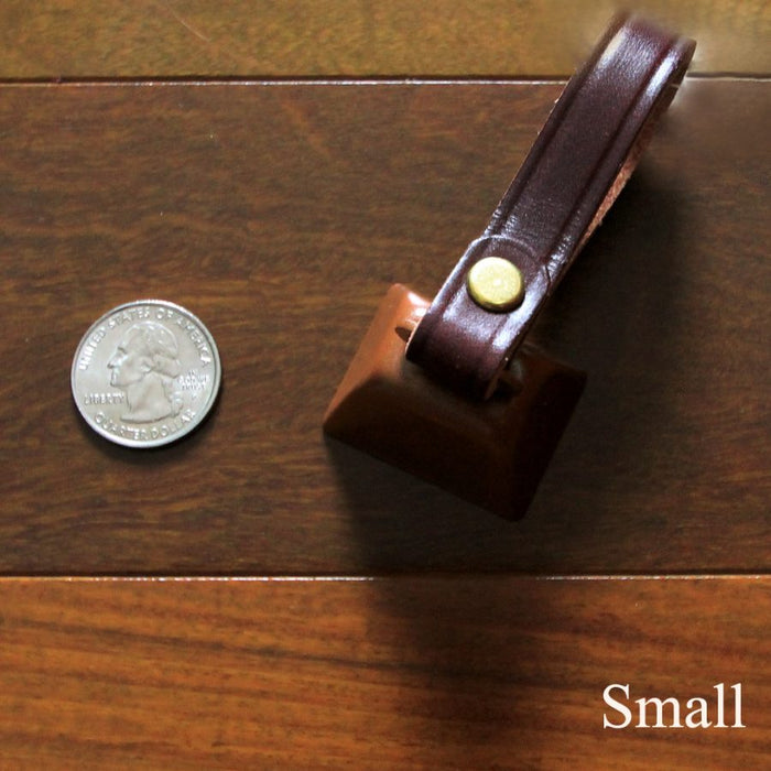 cowbell with antique brass finish and burgundy bridle leather strap shown next to a quarter
