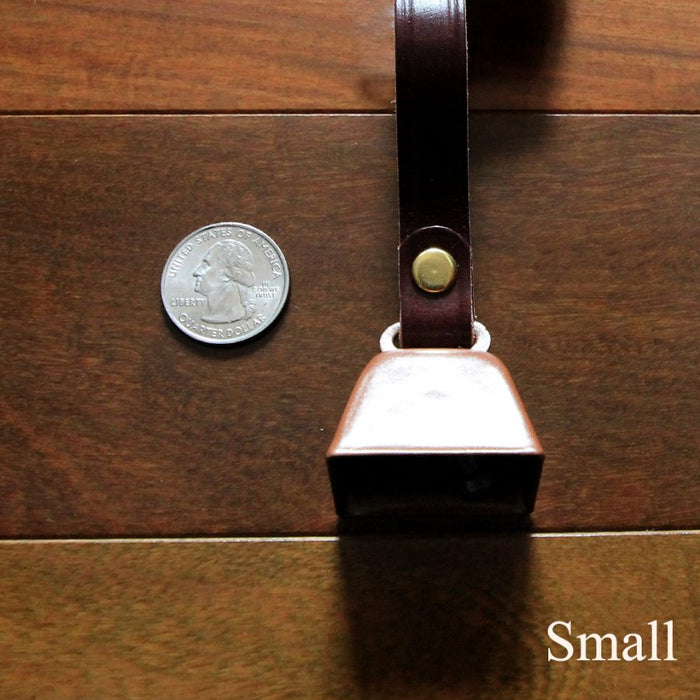 cowbell with antique brass finish and burgundy bridle leather strap shown next to a quarter