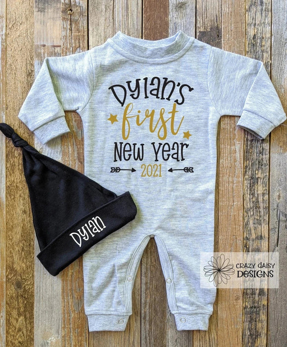Gray Baby Romper that says Dylan's First New Year in black and gold writing with a knot hat that has Dylan on it