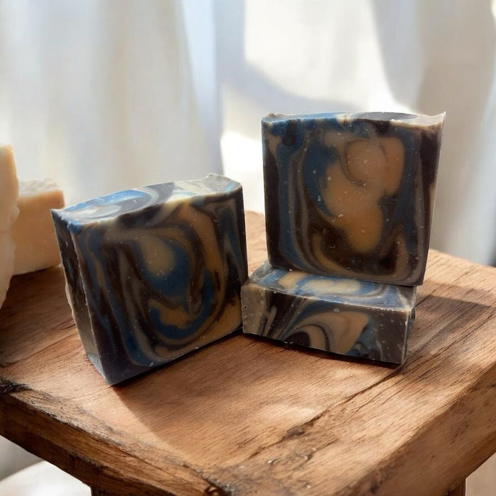 Three bars of Palo Santo scented bath and body soap with a swirled pattern of colors including blue and brown, displayed on a wooden surface.